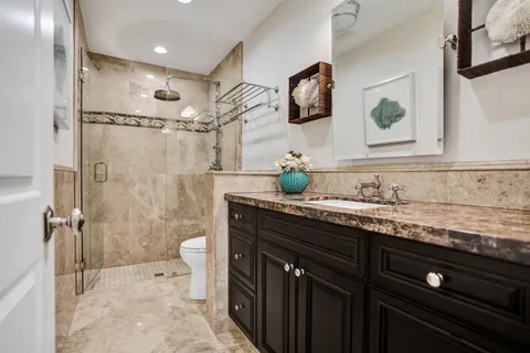 a bathroom with a granite countertop sink a toilet a mirror and shower