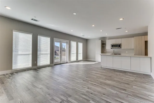 a view of an empty room with wooden floor and a kitchen