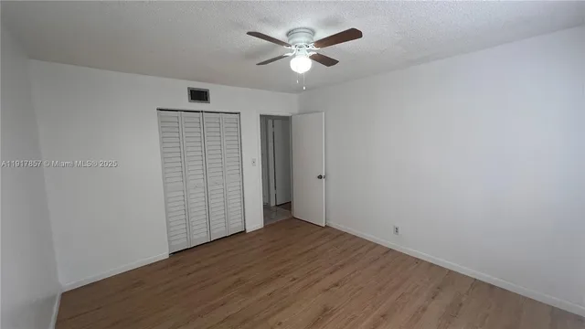 a view of an empty room with wooden floor and a ceiling fan