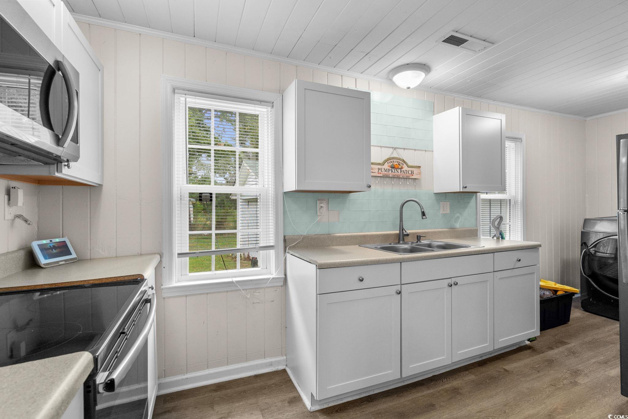 2475 Beverly Road Conway, SC 29527 - Photo 14 of 34 Kitchen featuring wooden walls, stainless steel appliances, dark wood-style flooring, light countertops, and white cabinetry