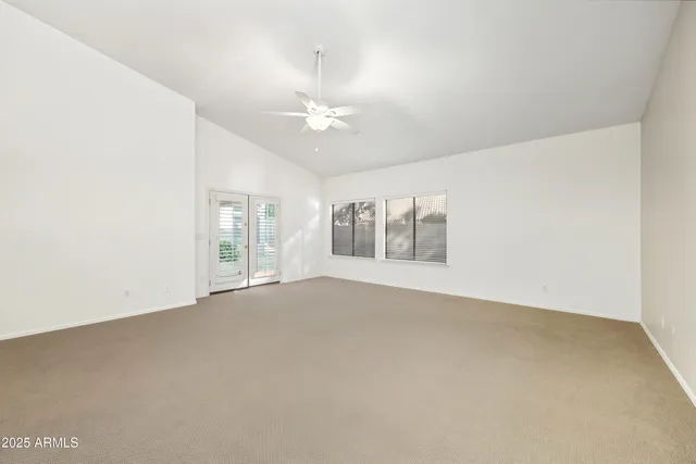 an empty room with chandelier fan and windows