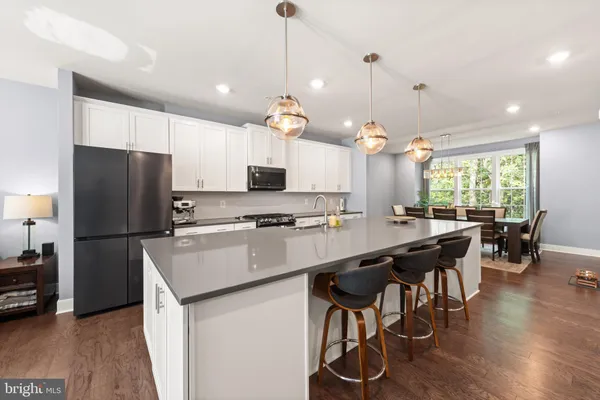 a kitchen with stainless steel appliances kitchen island a refrigerator a stove a dining table and chairs with wooden floor