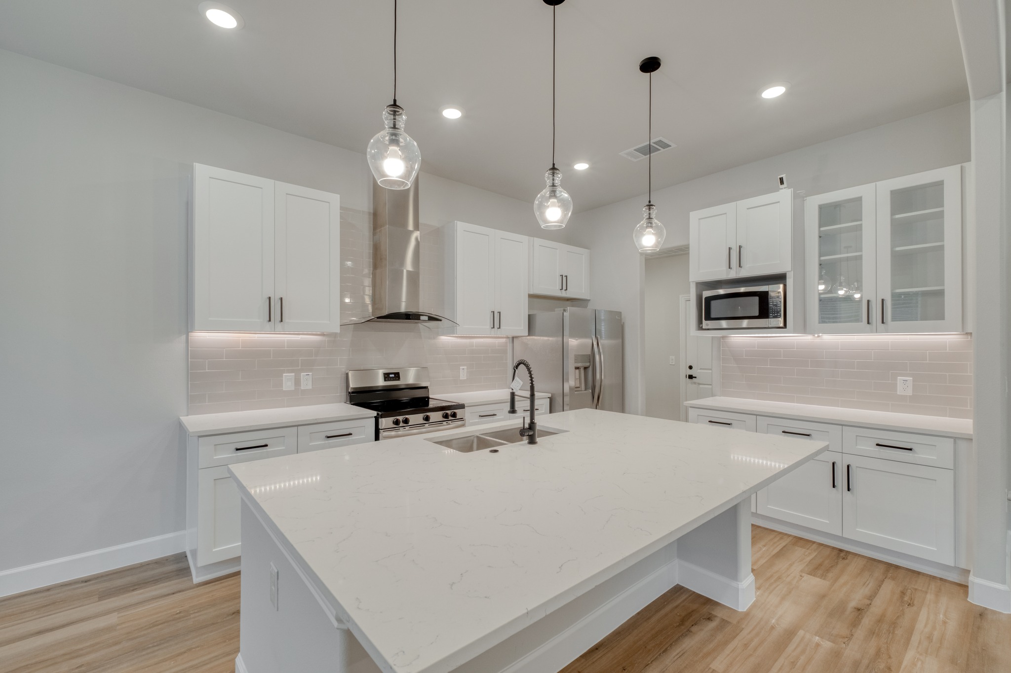 116 Pine Point Cove Elgin, TX 78621 - Photo 10 of 27 Bright kitchen featuring a substantial island, stainless steel appliances, white cabinetry, a subway tile backsplash, and wood-finish flooring