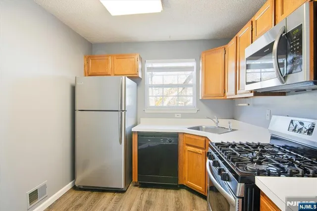 a kitchen with stainless steel appliances granite countertop a refrigerator a sink dishwasher a stove and a window with wooden floor