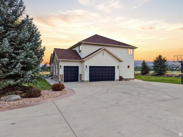 702 Alpine Highway Alpine, UT 84004 - Photo 77 of 83 Exterior featuring a stucco finish with stone accents, a multi-car garage with dark paneled doors, and mature evergreen landscaping