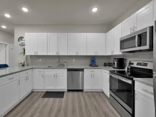 a kitchen with stainless steel appliances granite countertop a stove top oven a sink dishwasher and a microwave oven with white cabinets