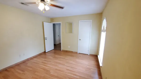 an empty room with a chandelier fan and wooden floor