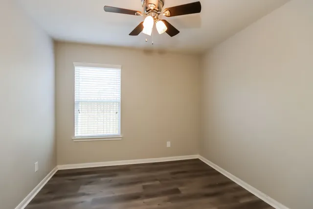 an empty room with wooden floor chandelier fan and windows