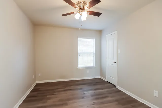 an empty room with wooden floor chandelier fan and windows