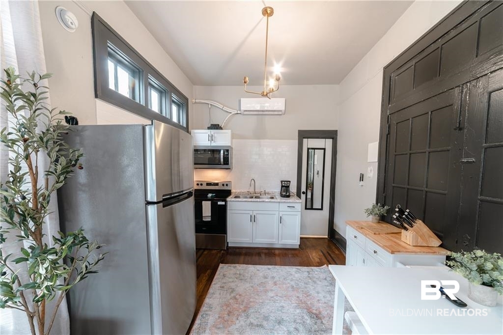 207 Michigan Avenue Mobile, AL 36604 - Photo 20 of 31 Kitchen featuring stainless steel appliances, dark wood-type flooring, white cabinetry, backsplash, and a chandelier