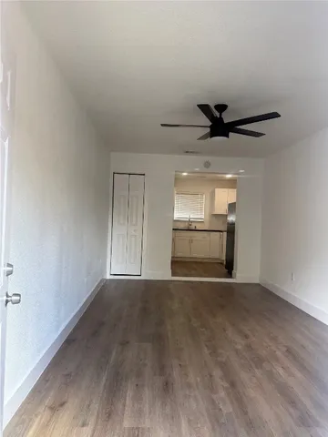 a view of an empty room and a kitchen with wooden floor