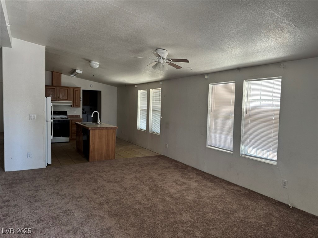 237 Piute Lane Henderson, NV 89015 - Photo 3 of 7 Unfurnished living room with light carpet, healthy amount of natural light, a ceiling fan, and a textured ceiling