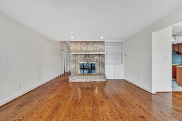 an empty room with wooden floor fireplace and windows