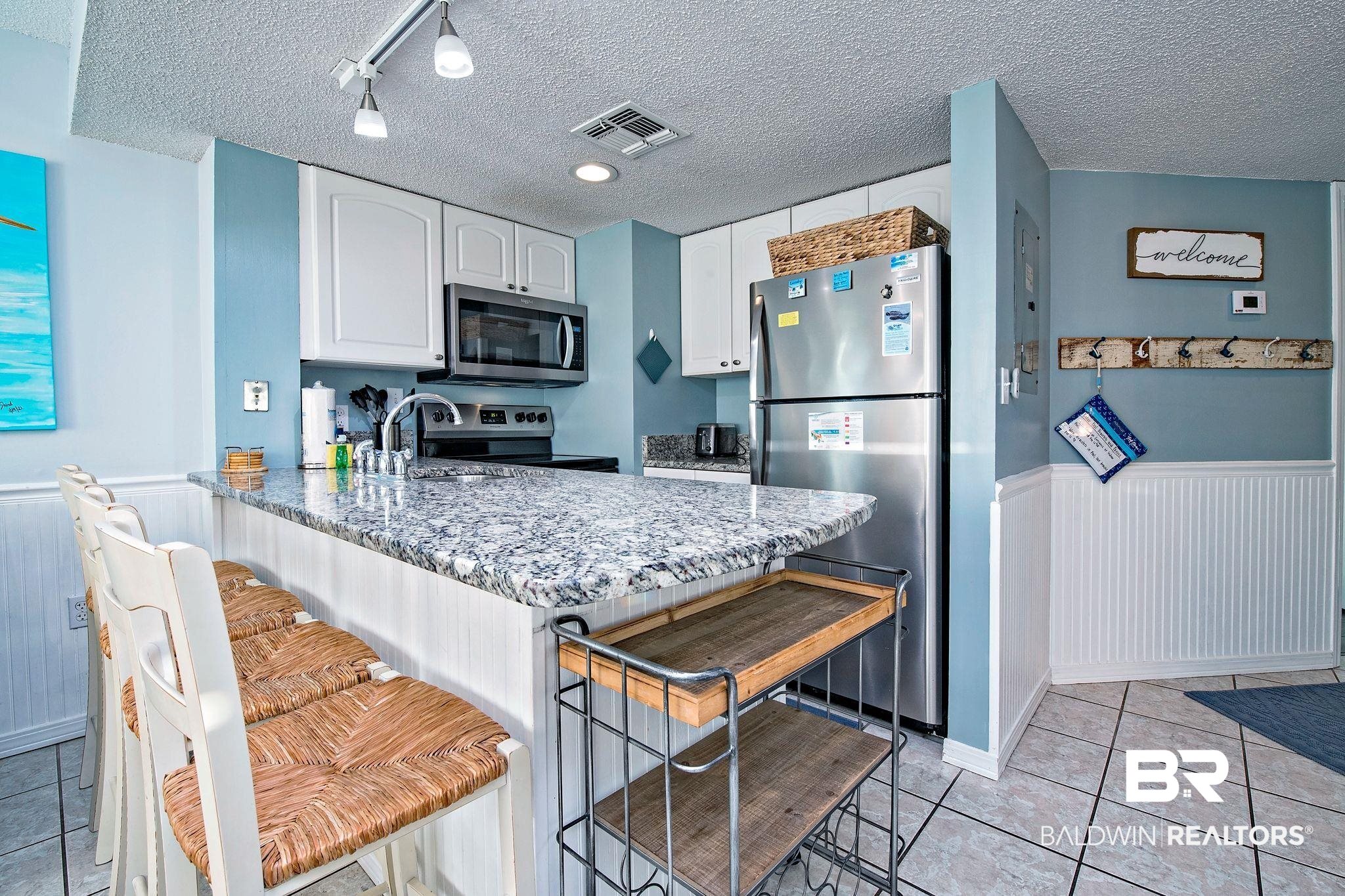 497 Plantation Road, Unit 1156 Gulf Shores, AL 36542 - Photo 3 of 28 Kitchen featuring sink, stainless steel appliances, a kitchen breakfast bar, light stone counters, and white cabinets
