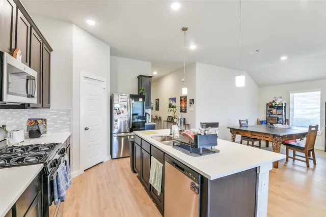 a kitchen with stainless steel appliances kitchen island granite countertop a table chairs in it and wooden floors
