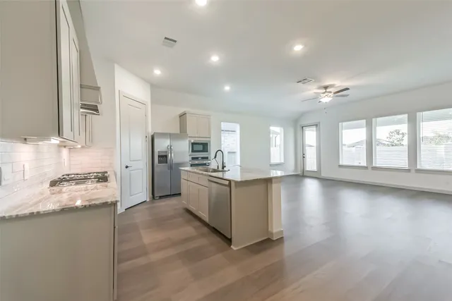 a kitchen with stainless steel appliances granite countertop a stove top oven a sink dishwasher a refrigerator and white cabinets with wooden floor