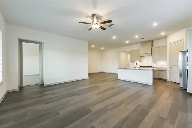 a view of an empty room with wooden floor and a kitchen
