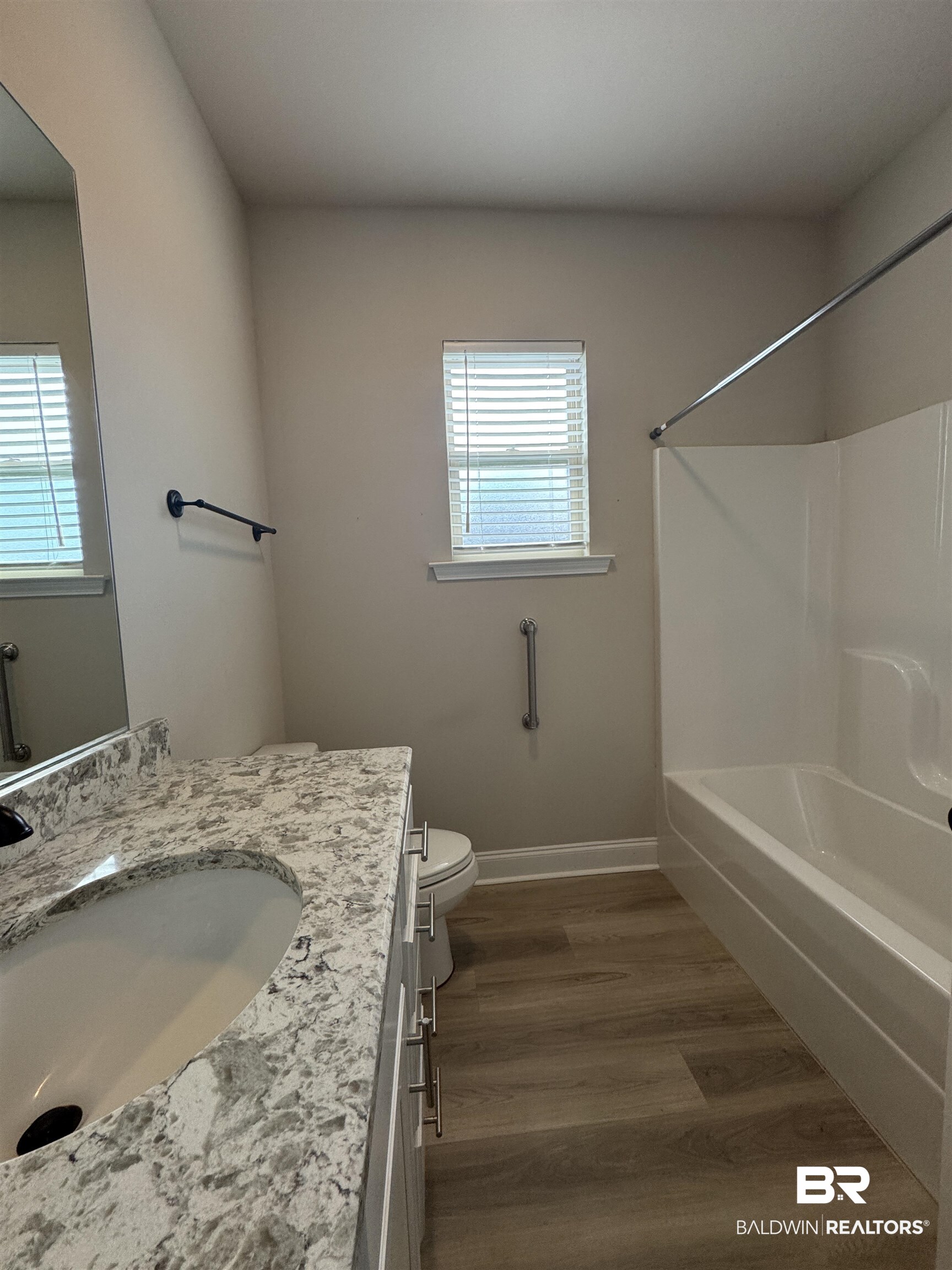 1060 Chloe Street Foley, AL 36535 - Photo 20 of 28 Bathroom featuring a vanity with an integrated sink and light-colored countertop, a white bathtub with a shower kit, a toilet, a window with blinds, and wood-finish flooring