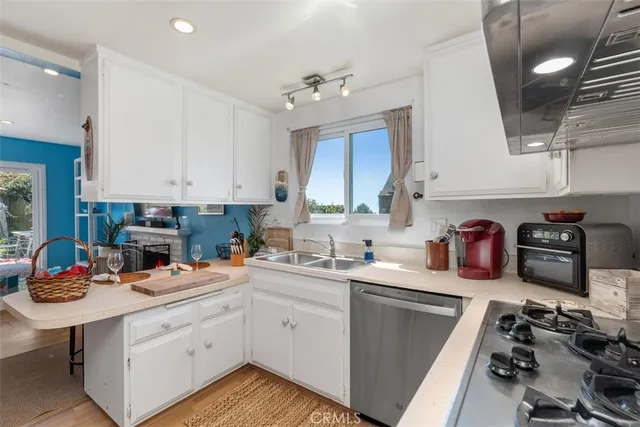 a kitchen with a sink dishwasher stove and white cabinets next to a window