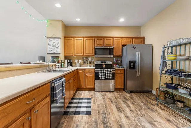 a kitchen with stainless steel appliances granite countertop a sink a stove a refrigerator and island with wooden cabinets