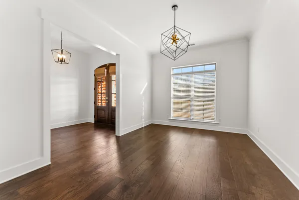an empty room with wooden floor chandelier and windows