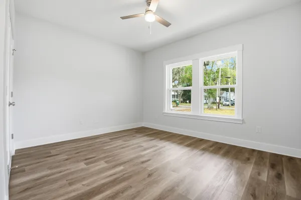 a view of an empty room with wooden floor and a ceiling fan