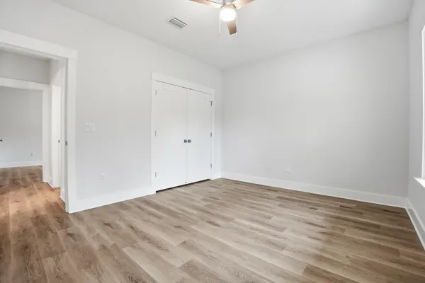 an empty room with wooden floor chandelier fan and windows