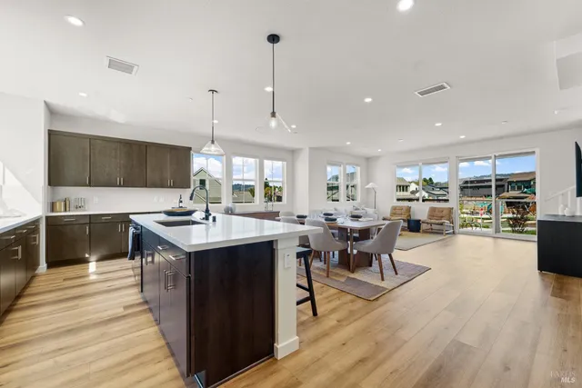 a open kitchen with stainless steel appliances granite countertop a sink dishwasher a stove and a dining table with wooden floor