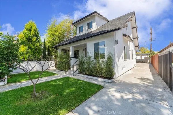 a view of a white house next to a yard with potted plants
