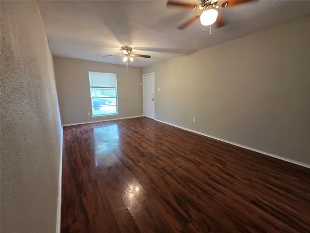 an empty room with wooden floor chandelier fan and windows
