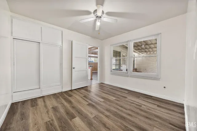 an empty room with wooden floor chandelier fan and windows