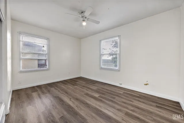 an empty room with wooden floor chandelier fan and windows