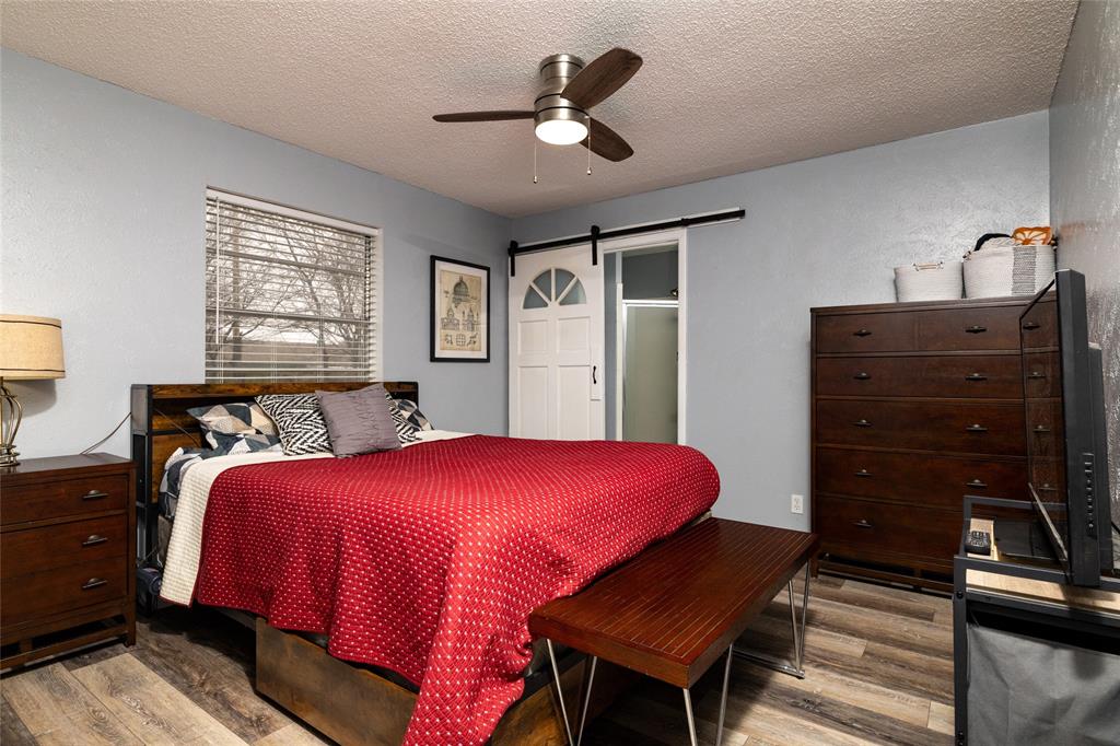 6020 Harrison Way Watauga, TX 76148 - Photo 20 of 32 Bedroom featuring a textured ceiling, a ceiling fan, a barn door, and light wood-type flooring