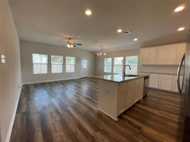 a living room with kitchen island granite countertop wooden floors and white cabinets