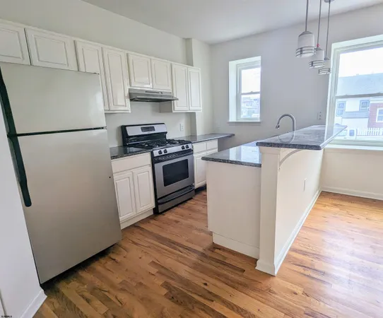 a kitchen with stainless steel appliances granite countertop a refrigerator a stove a sink and white cabinets with wooden floors