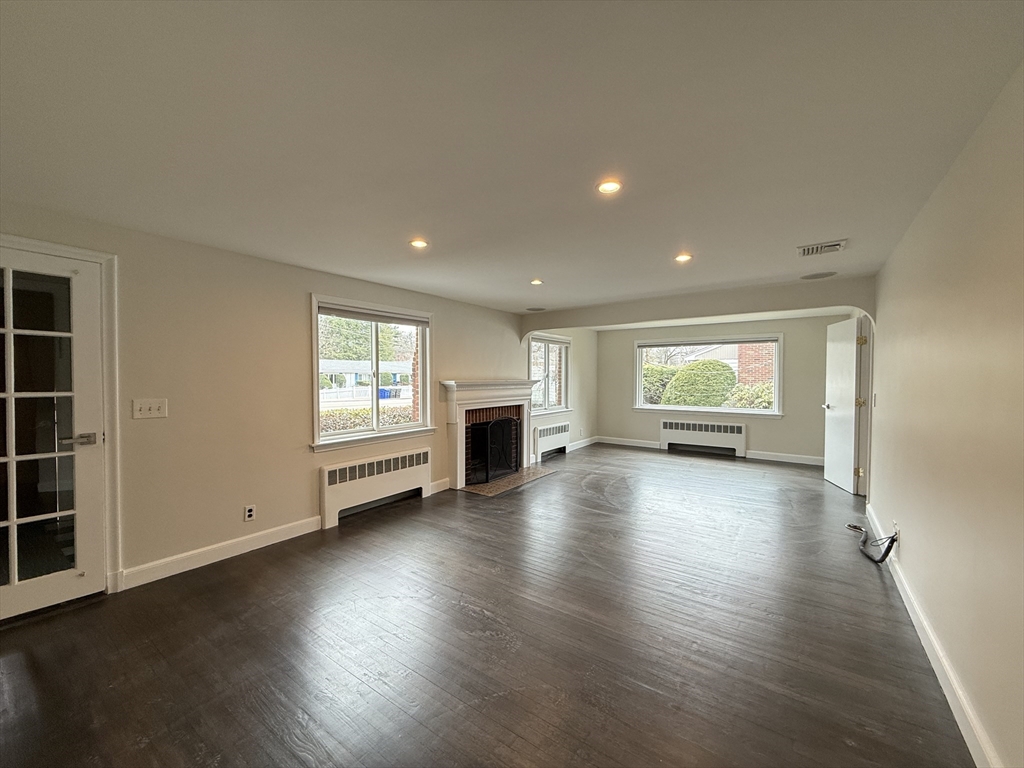 115 Grove Street Brookline, MA 02467 - Photo 4 of 12 an empty room with wooden floor fireplace and windows