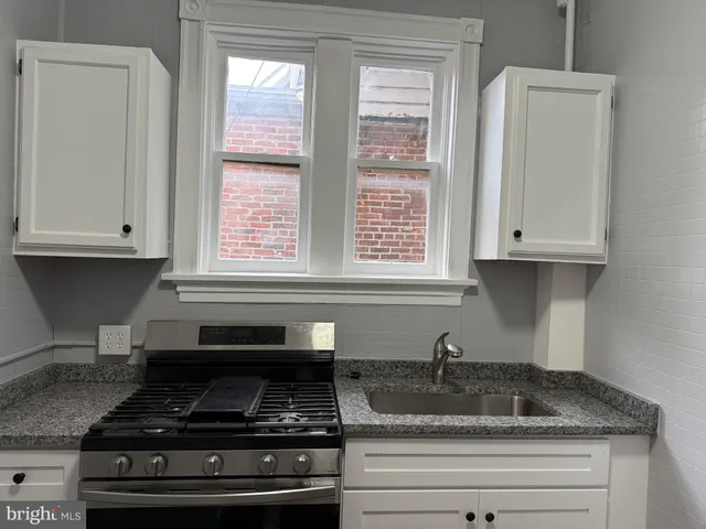a kitchen with granite countertop white cabinets and a stove a sink