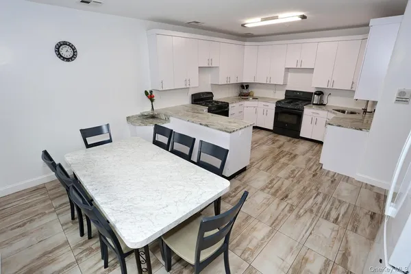 a kitchen with stainless steel appliances granite countertop a stove a sink a refrigerator and white cabinets with wooden floor