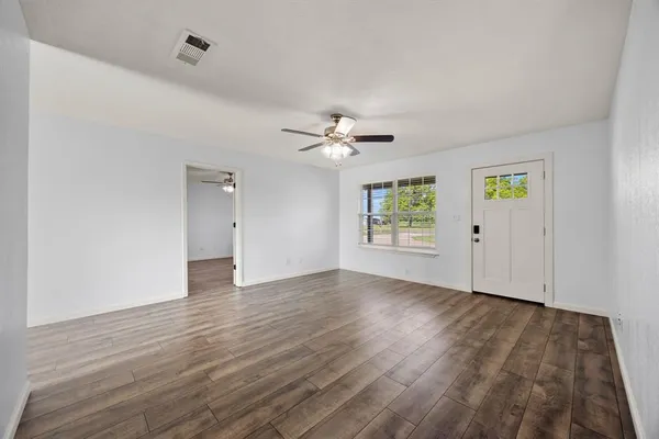 an empty room with wooden floor chandelier fan and windows