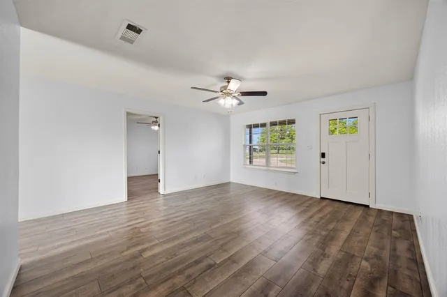 an empty room with wooden floor chandelier fan and windows