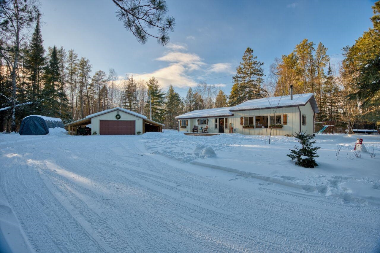 View of front facade with an outbuilding, a garage, view of wooded area, board and batten siding, and a deck