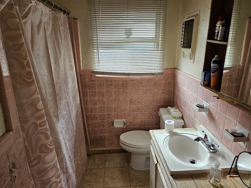 2714 Crest Ridge Drive Dallas, TX 75228 - Photo 11 of 15 Bathroom featuring pink tiled walls, a white toilet, a single vanity with a white basin and chrome faucet, and a window with horizontal blinds