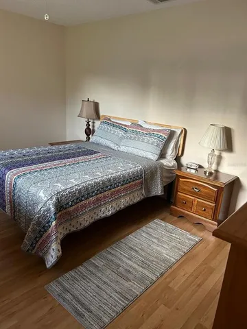 a bedroom with a bed wooden floor and view of living room