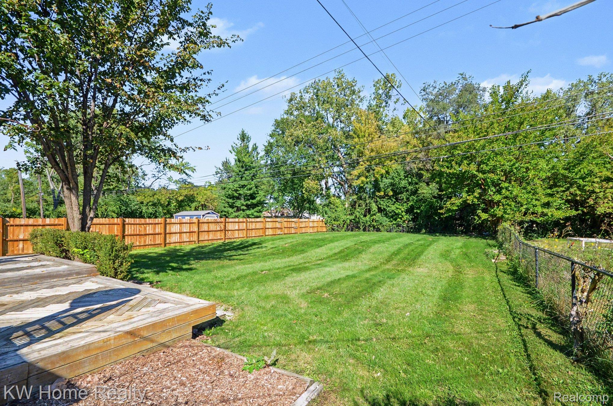 2383 East Maple Road Troy, MI 48083 - Photo 20 of 25 Expansive backyard featuring a wood deck, manicured lawn, wood privacy fence, and chain-link fence
