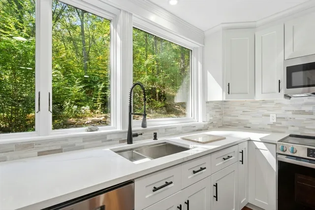 a kitchen with sink a large window appliances and cabinets