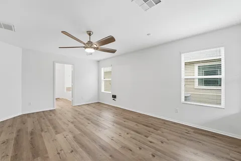 a view of an empty room with wooden floor and a ceiling fan