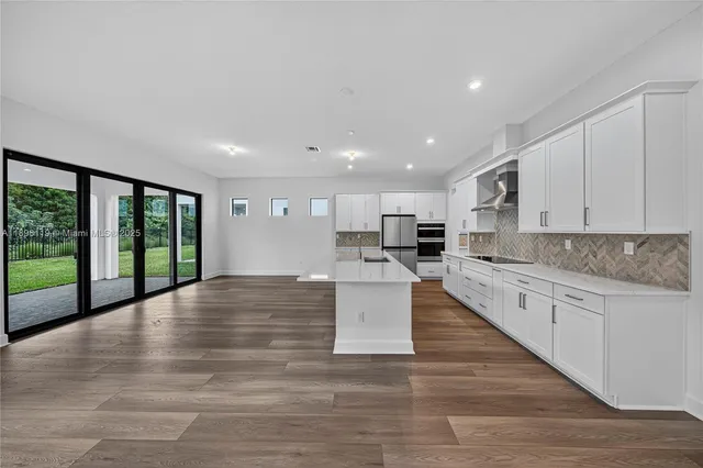 a large white kitchen with kitchen island a large window a sink and cabinets