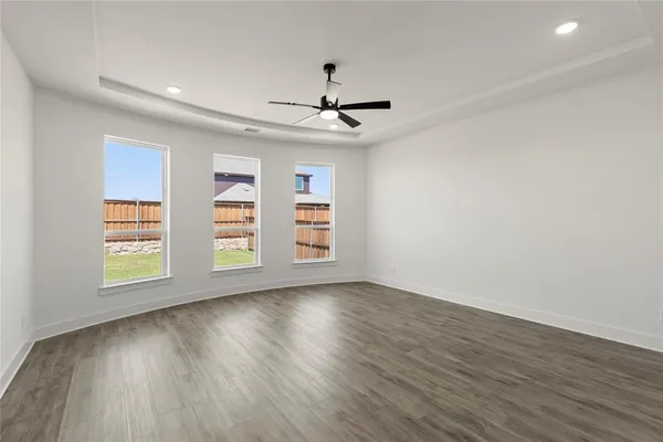 an empty room with wooden floor ceiling fan and windows