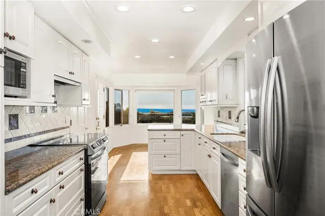 a large white kitchen with stainless steel appliances granite countertop a refrigerator a sink dishwasher a stove and white cabinets with wooden floor