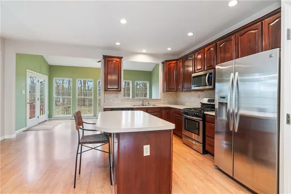 a kitchen with stainless steel appliances granite countertop a refrigerator a stove a sink a dining table and chairs with wooden floor